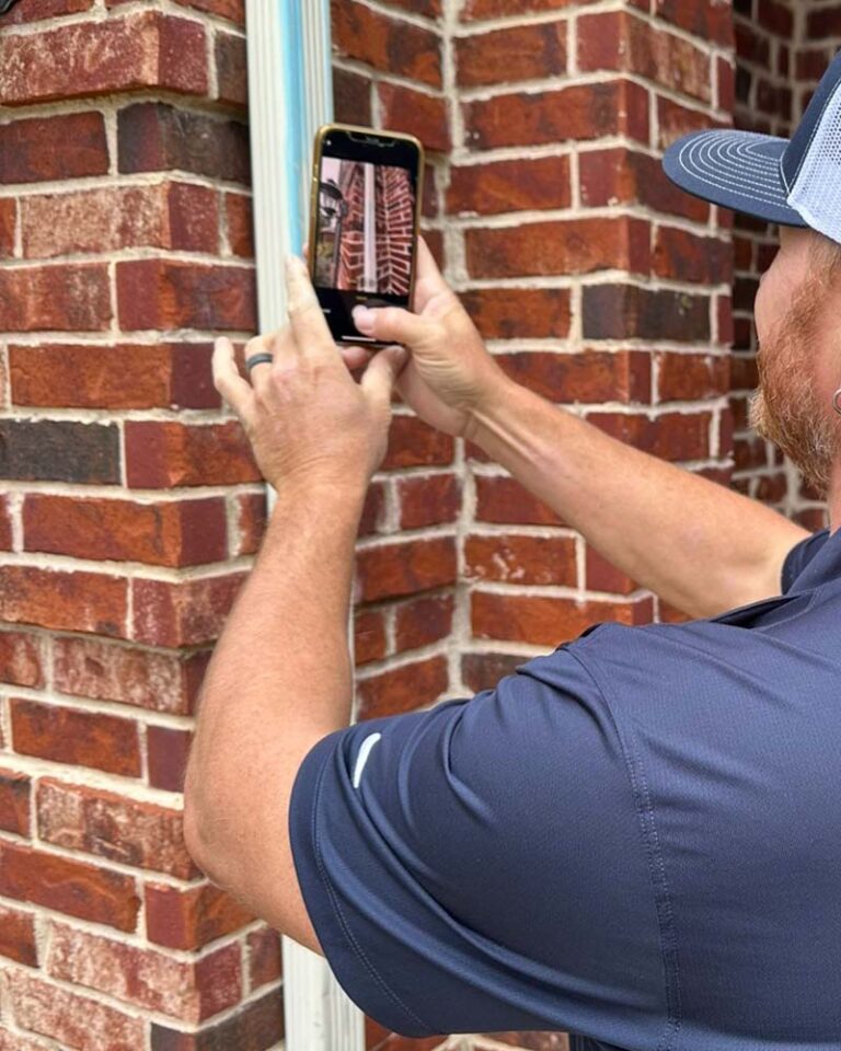 A man taking a picture of a brick wall with a cell phone.