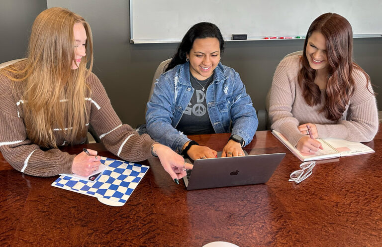 Three women sitting around a table with laptops.